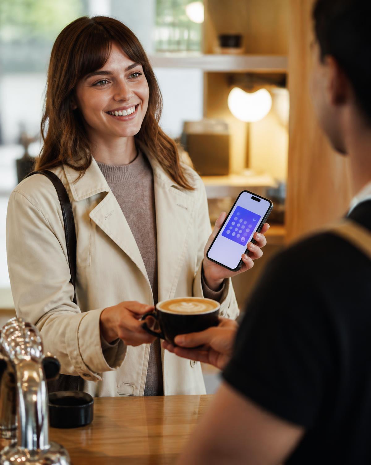 A regular customer receiving a coffee while holding a digital loyalty card on her phone